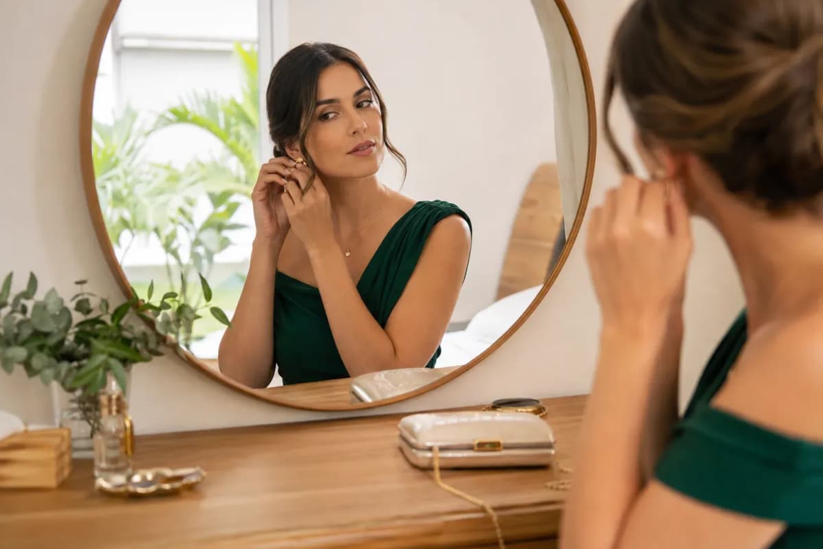 Invitada con vestido verde ajustándose aretes frente a un espejo antes de una boda