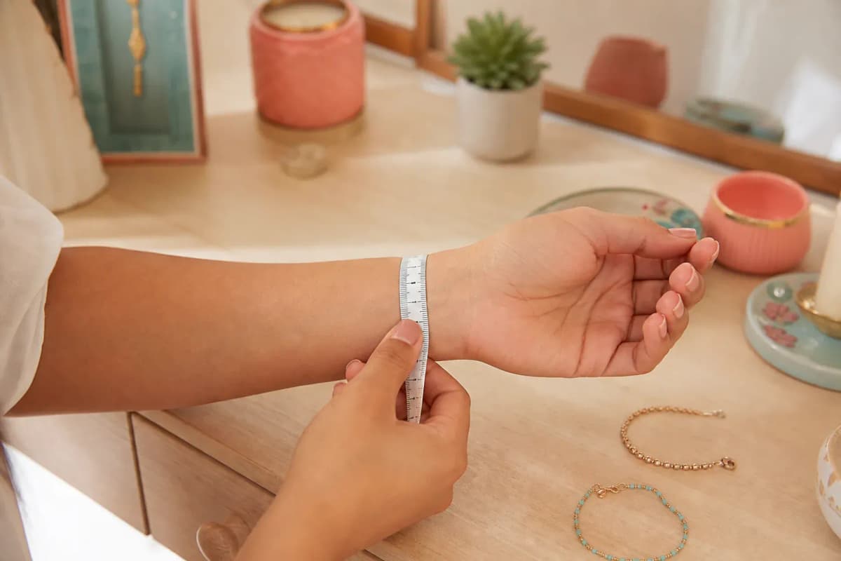 Manos midiendo una muñeca con cinta métrica junto a una pulsera y una tobillera